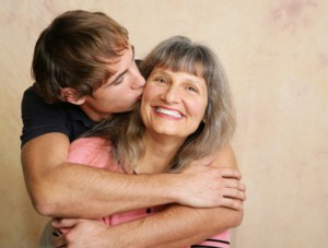 Young adult/late teen son kissing his mother on the cheek.